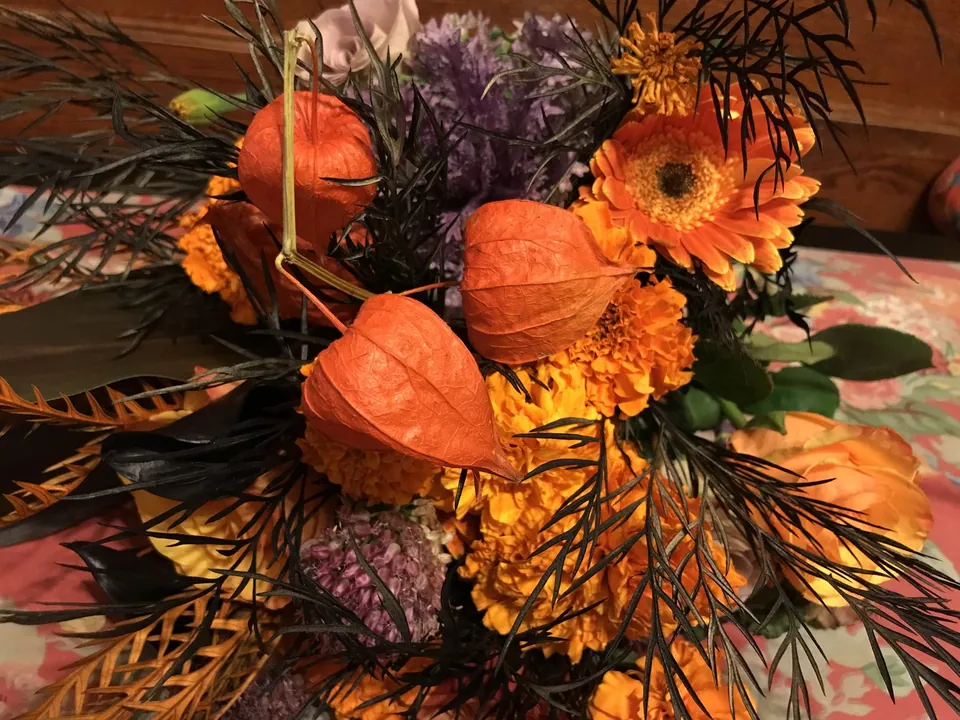 Autumn table flowers with small pumpkins, purple hydrangea, orange gerbera, and twig texture.