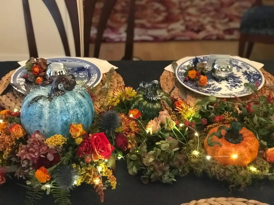 Blue and orange pumpkin table centerpiece with fall flowers, greenery, and candlelight.