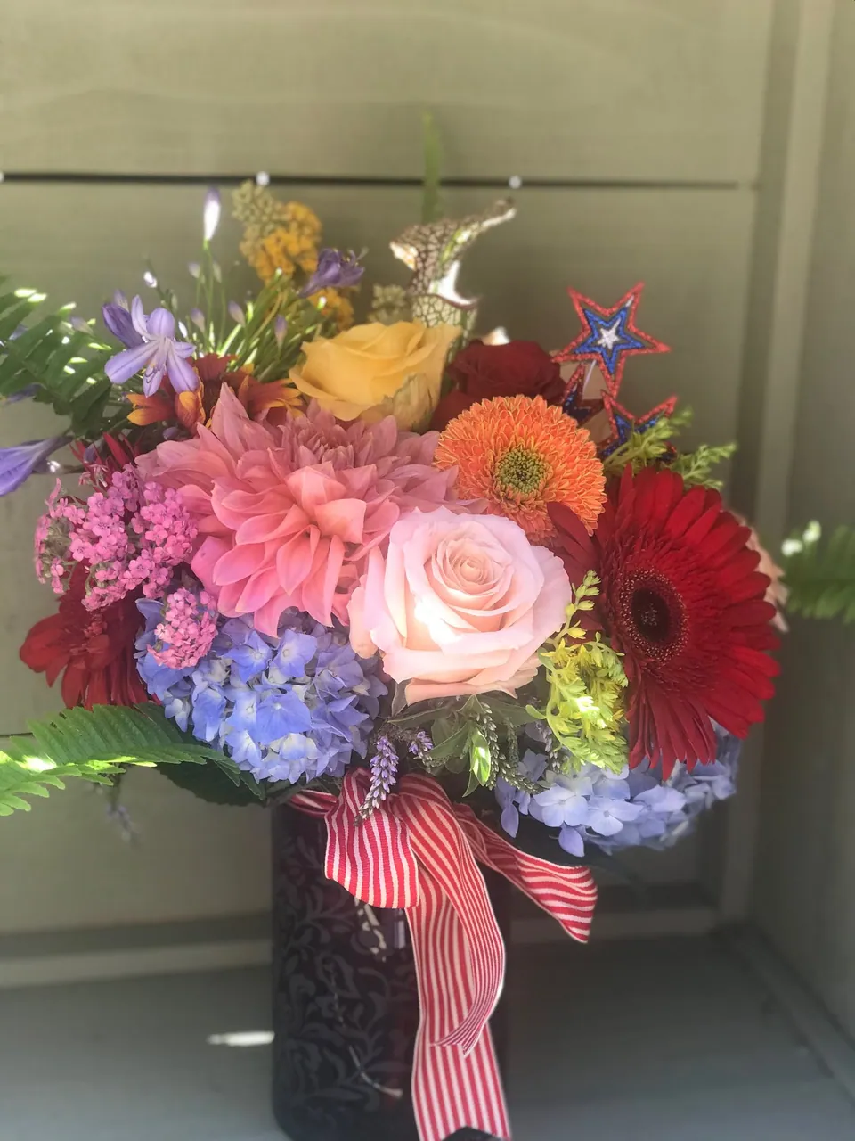Bright red, yellow, blue, and pink arrangement with striped ribbon and summer flowers.