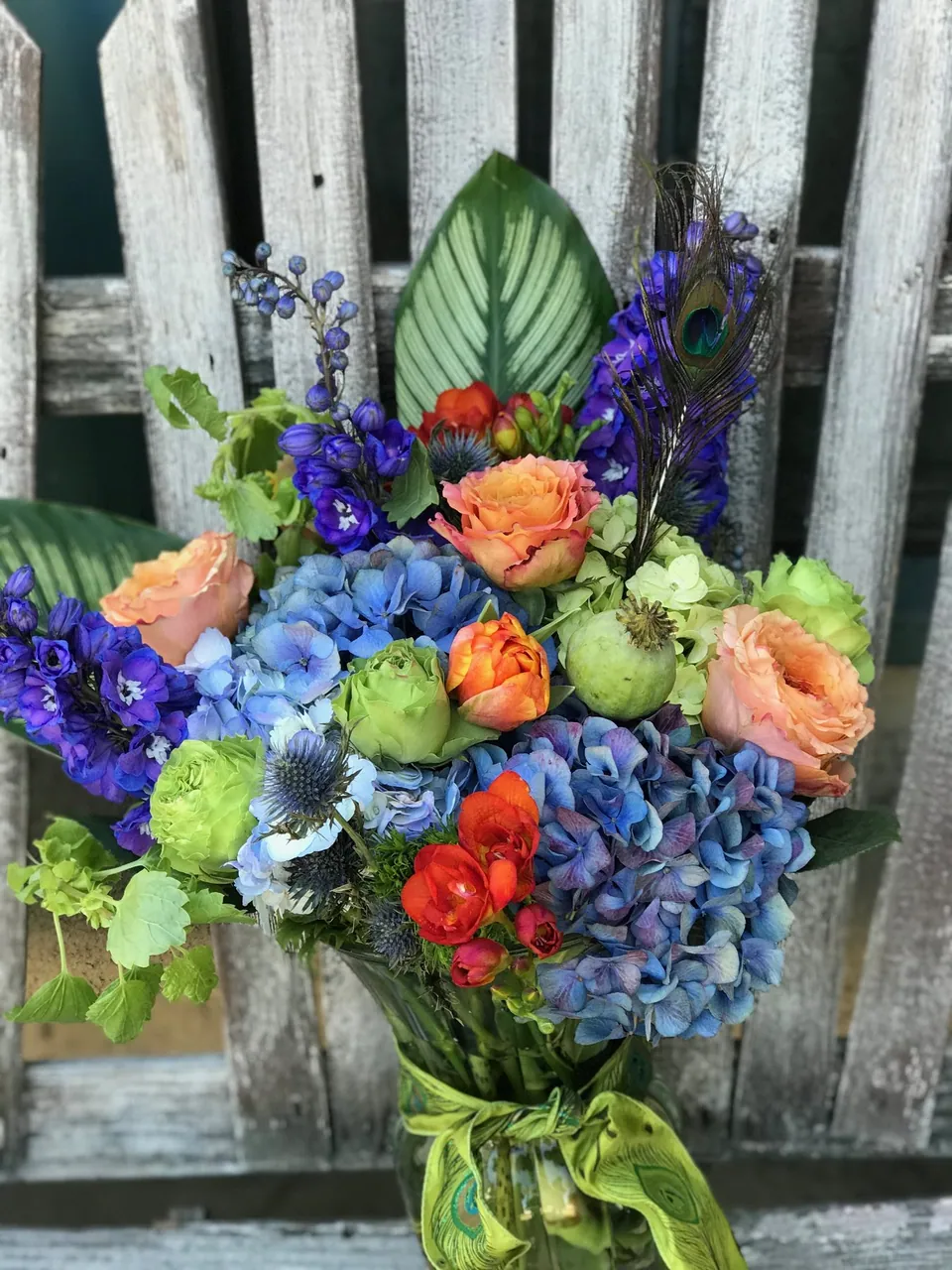 Colorful bouquet with blue hydrangea, orange roses, and green textured accents.