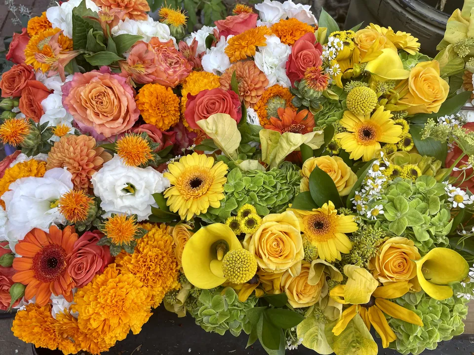Large yellow, orange, ivory, and coral celebration flowers with roses and sunflowers.