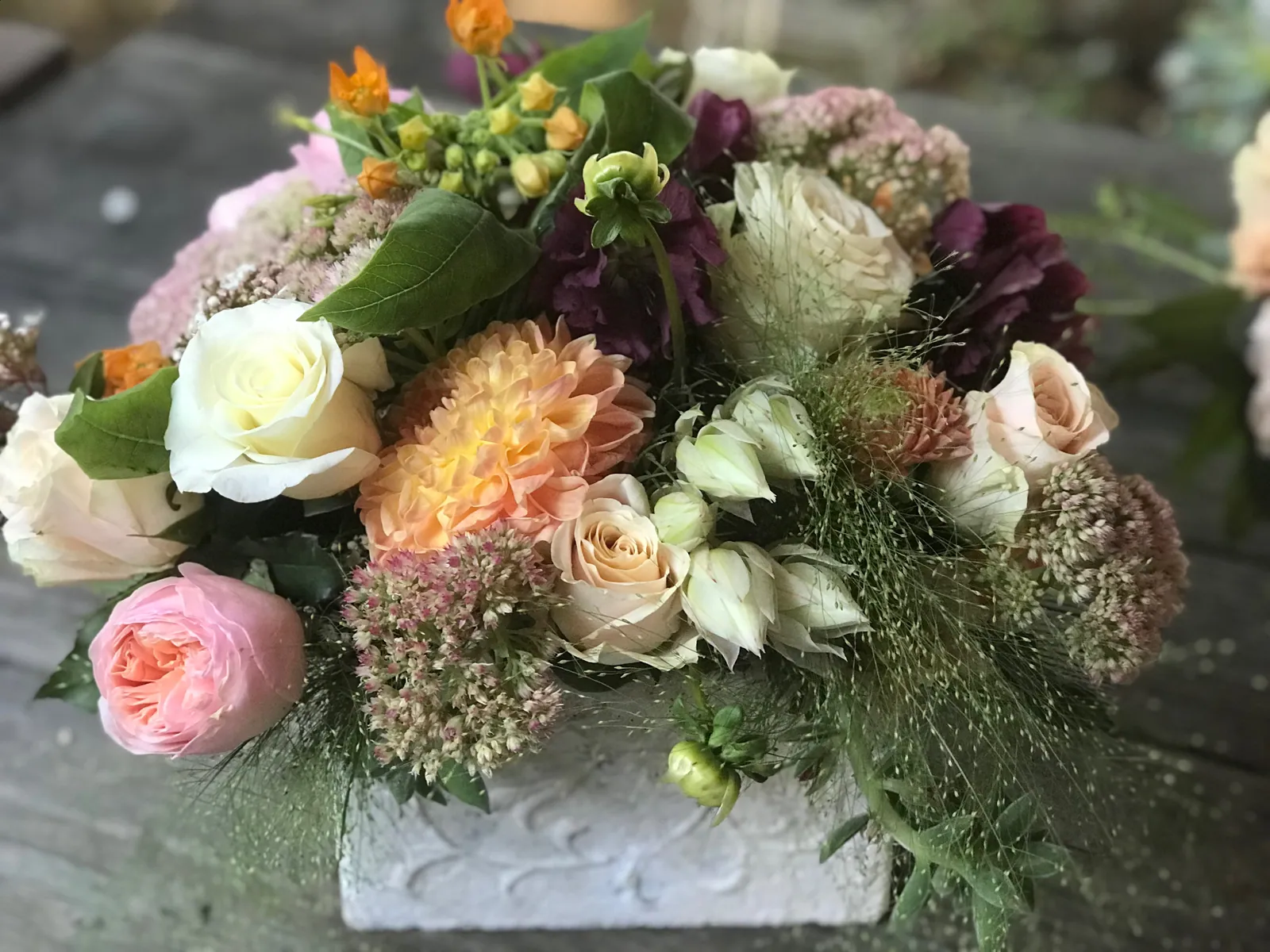 Low garden style floral arrangement with roses, pale hydrangea, texture, and greenery.