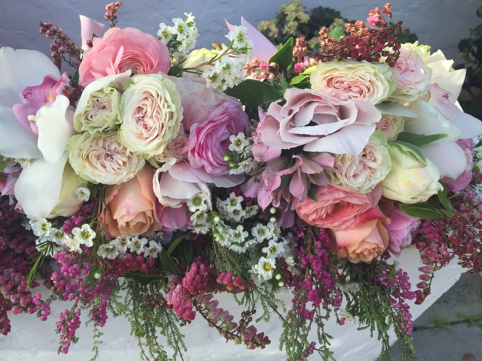 Lush romantic table florals with pale pink roses, mauve blooms, and trailing purple flowers.