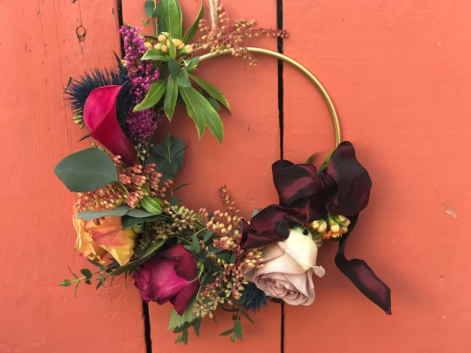 Modern wreath floral piece with burgundy orchids, berries, and ribbon.
