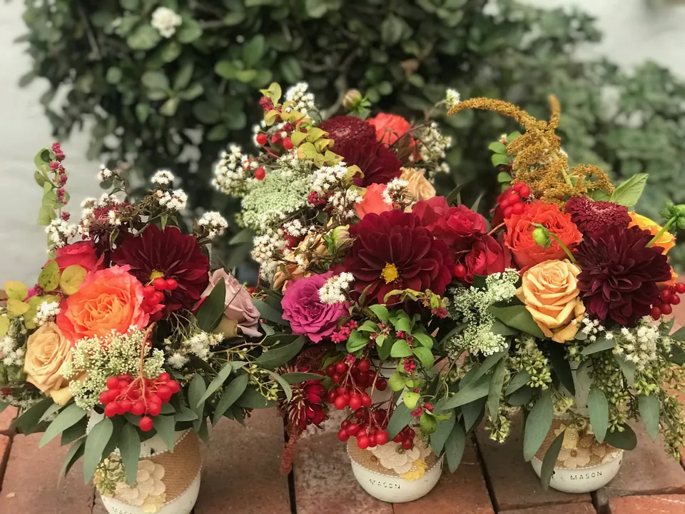Pair of autumn floral vessels with roses, berries, orange orchids, and trailing greenery.