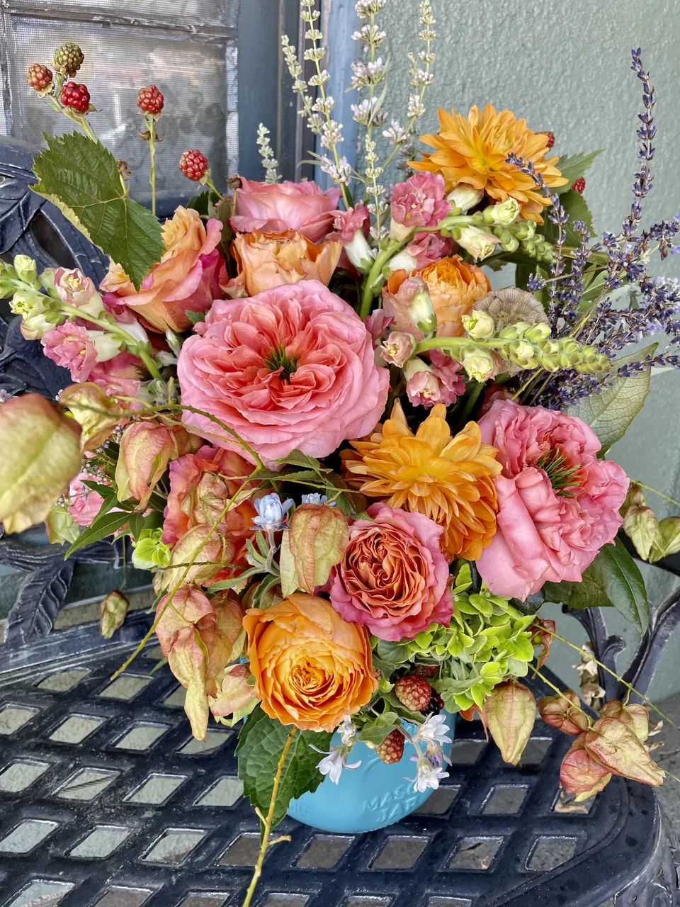 Pink and orange floral arrangement in a blue vessel with orchids, roses, and soft greenery.