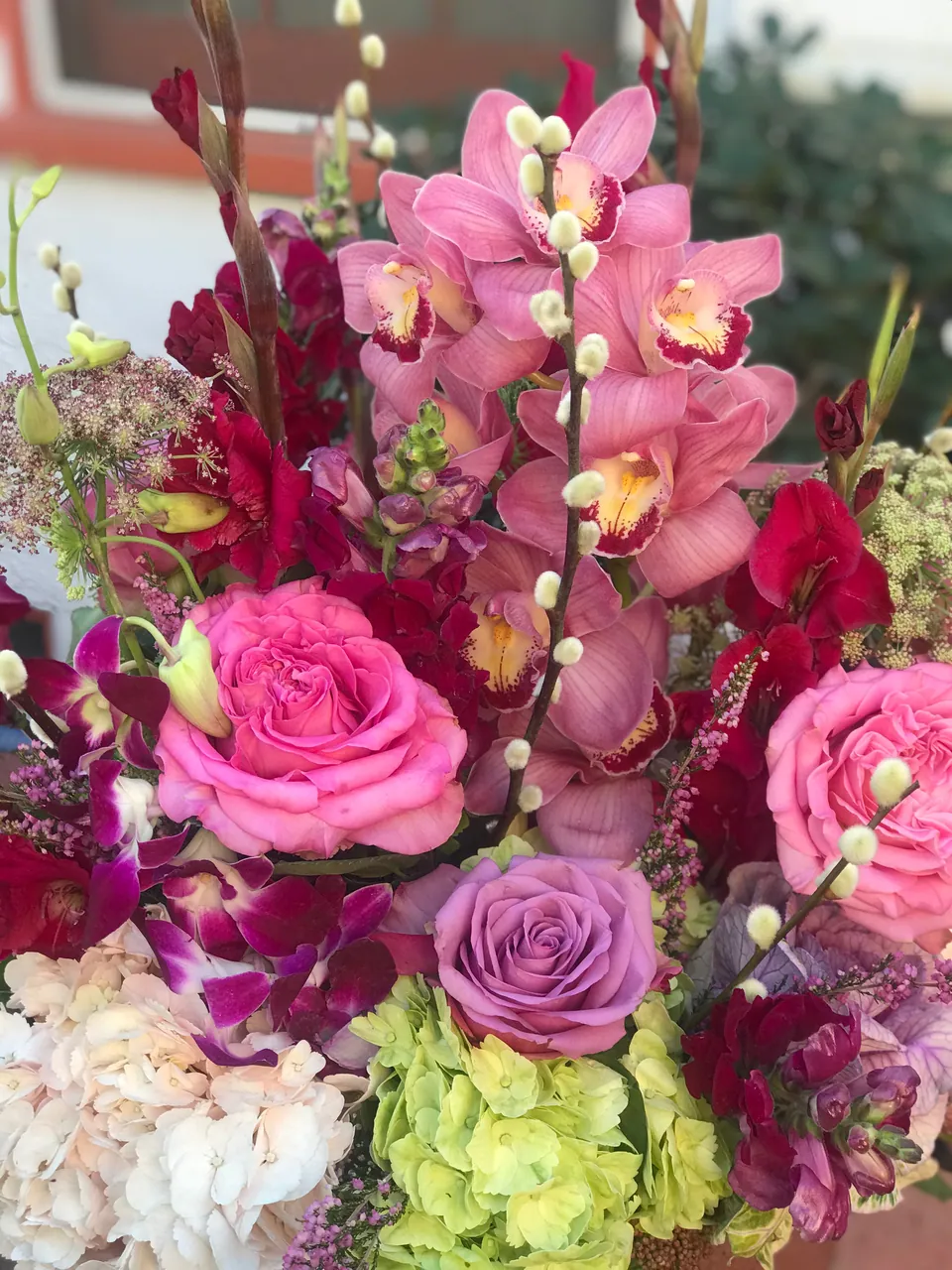 Pink, purple, and chartreuse arrangement with orchids, roses, and hydrangea texture.