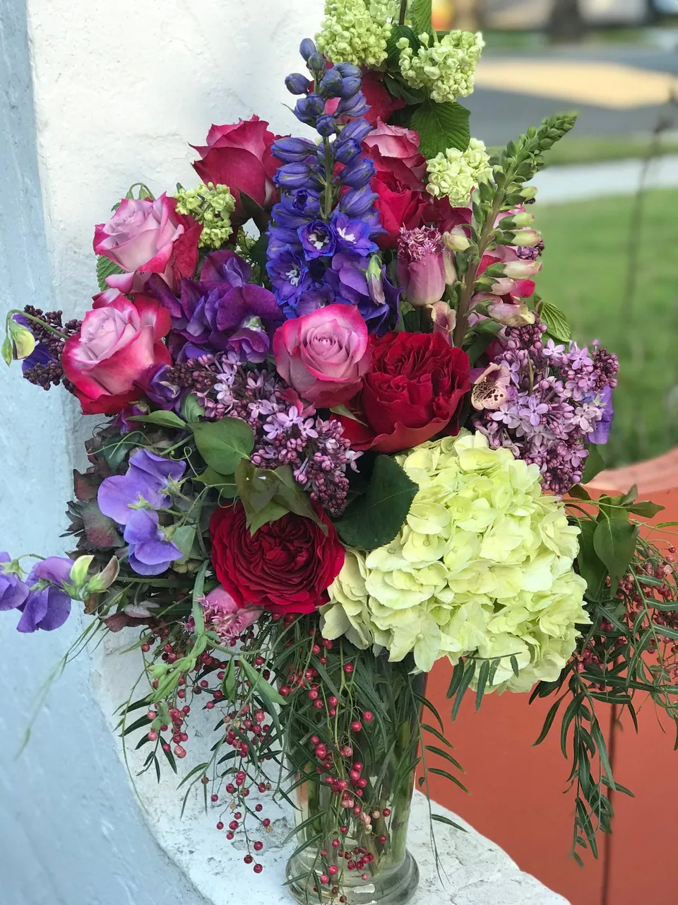 Purple, red, peach, and green garden bouquet with hydrangea, roses, and loose greenery.