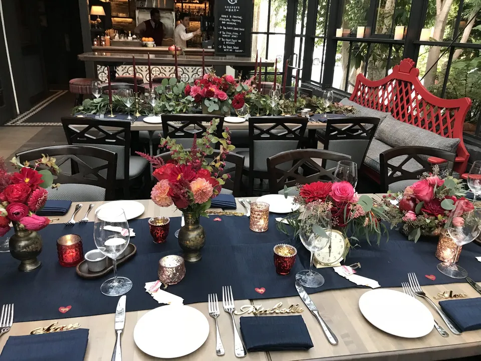 Long reception table with red and pink floral arrangements and candlelight.