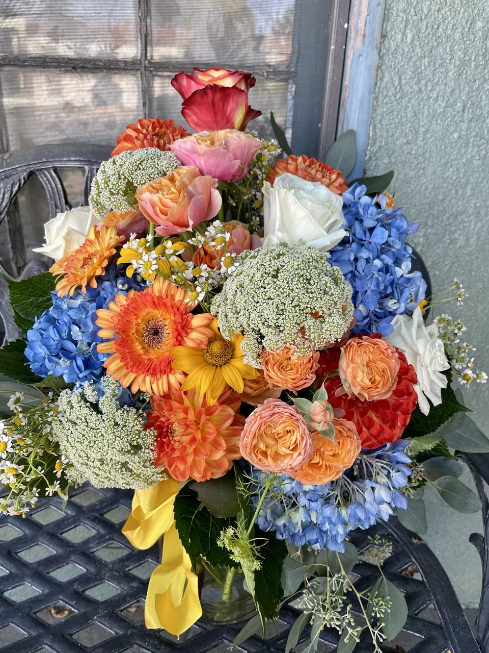 Round blue, peach, orange, and yellow garden arrangement with hydrangea and roses.