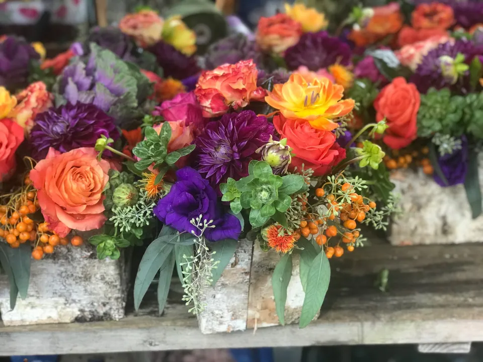 Row of small colorful floral vessels with orange, purple, pink, and red flowers.