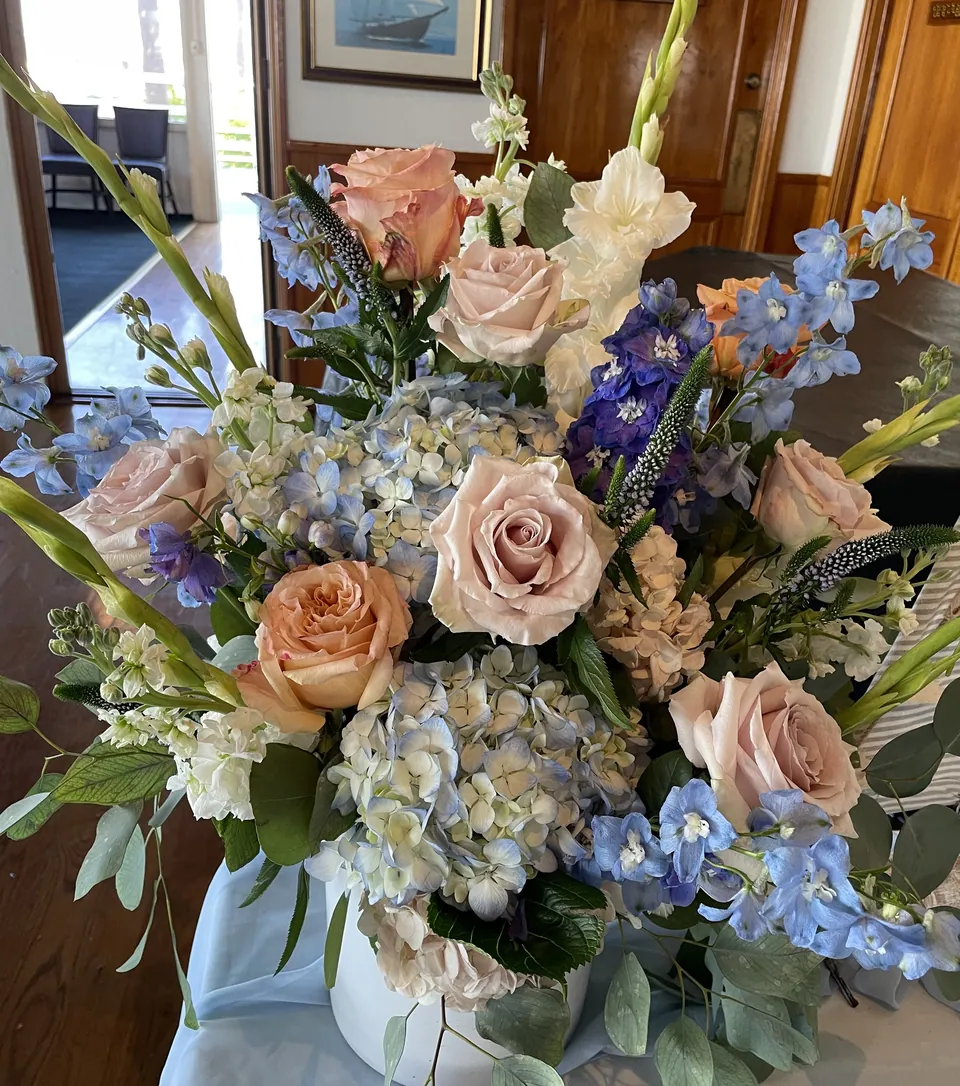 Soft blue, blush, cream, and green romantic floral arrangement with roses and airy movement.