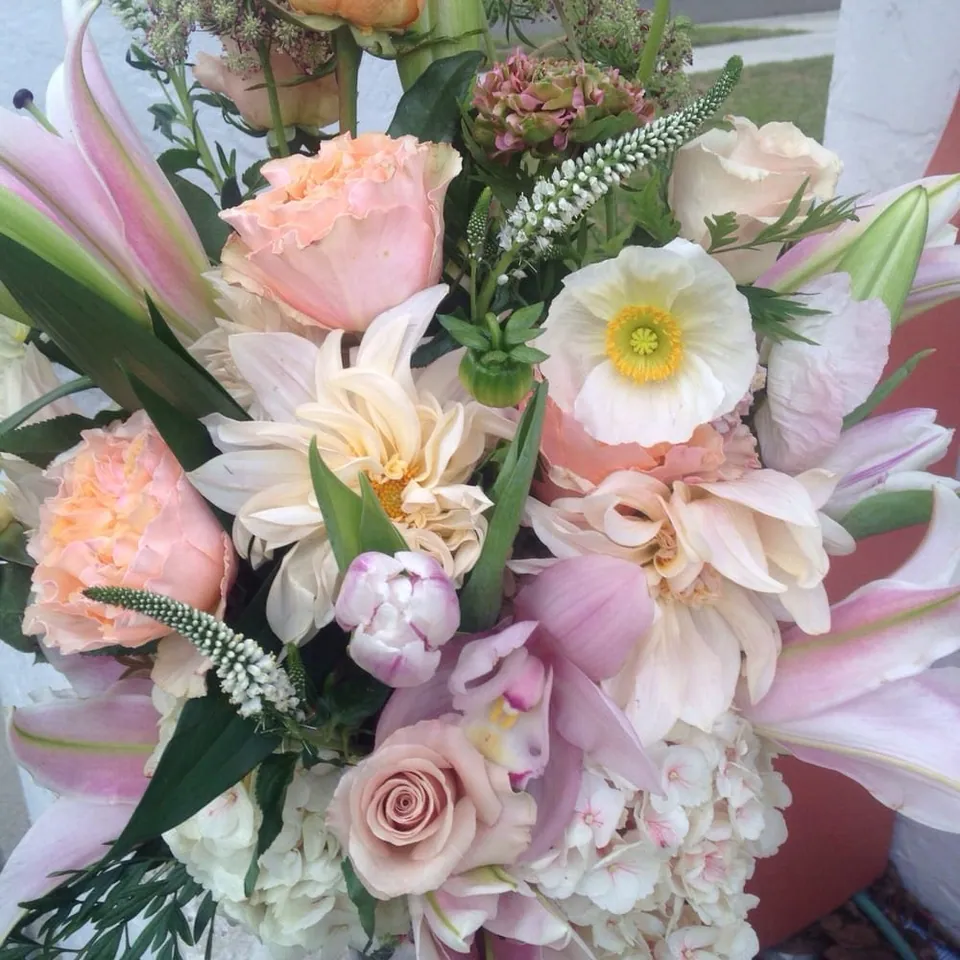 Soft bouquet with lilies, roses, white flowers, and pale blush tones.