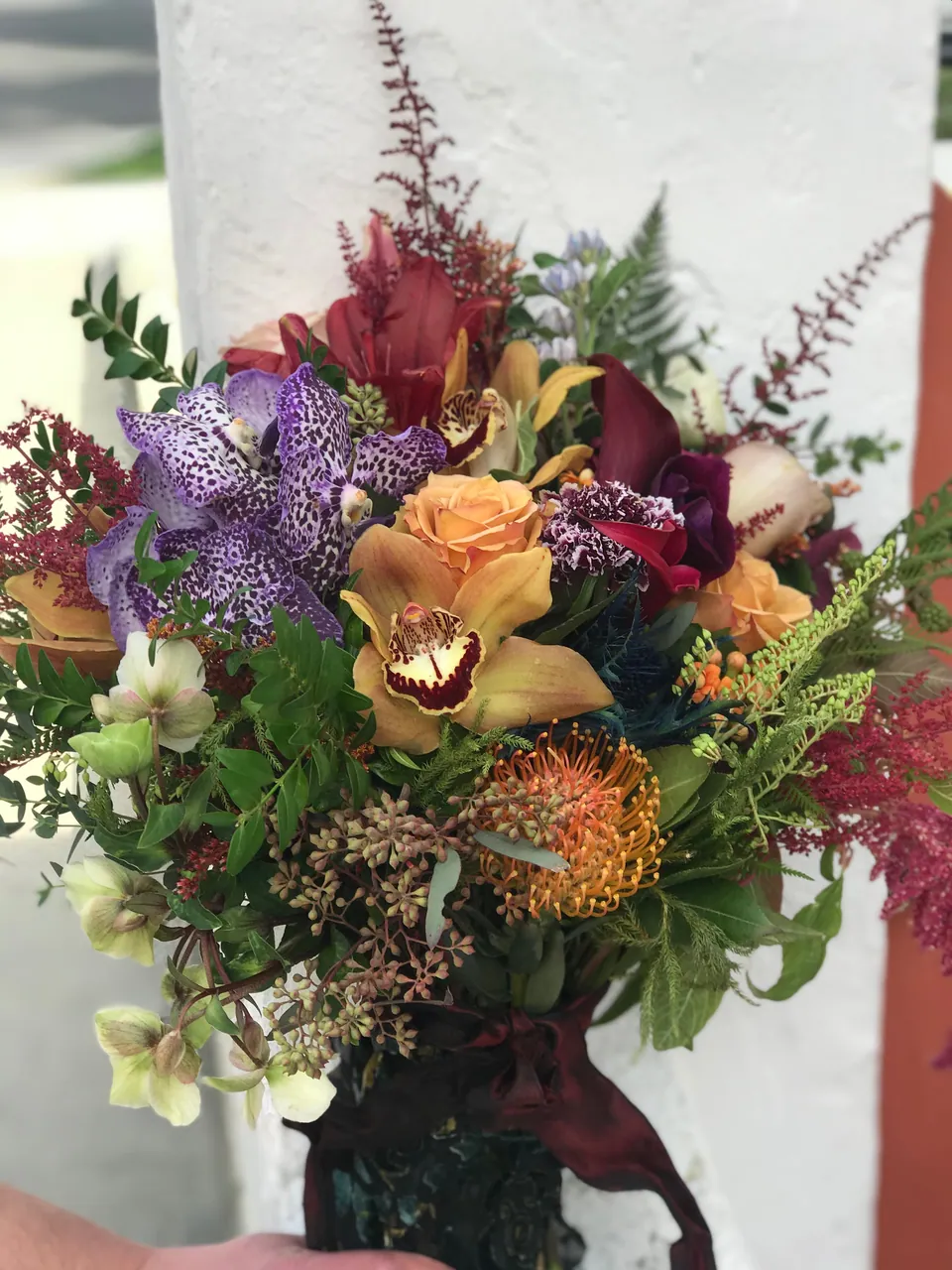 Textured garden arrangement with citrus, burgundy flowers, peach roses, and greenery.