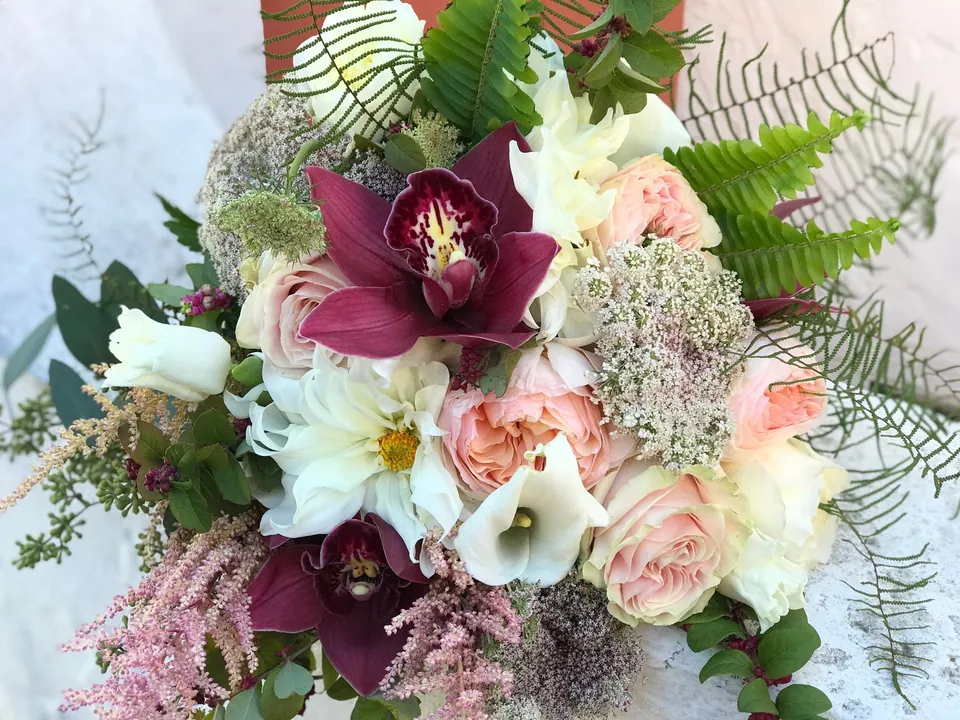 White, blush, and burgundy bouquet with orchids, roses, and fern texture.